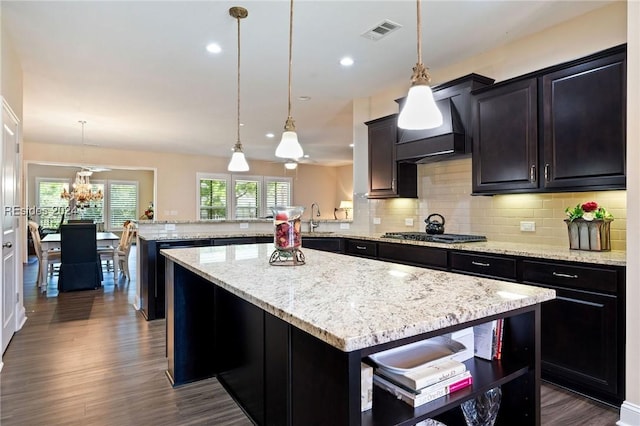 kitchen with custom exhaust hood, decorative light fixtures, kitchen peninsula, a kitchen island, and stainless steel gas stovetop