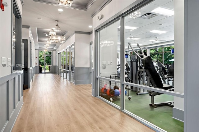 exercise room featuring an inviting chandelier, ornamental molding, a healthy amount of sunlight, and light wood-type flooring