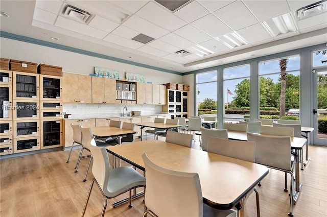 dining room with sink, a paneled ceiling, wine cooler, a raised ceiling, and light wood-type flooring