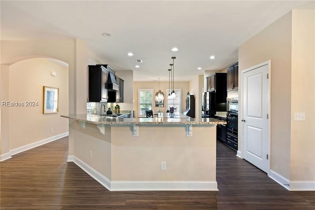 kitchen with decorative light fixtures, a breakfast bar area, dark hardwood / wood-style flooring, kitchen peninsula, and light stone countertops