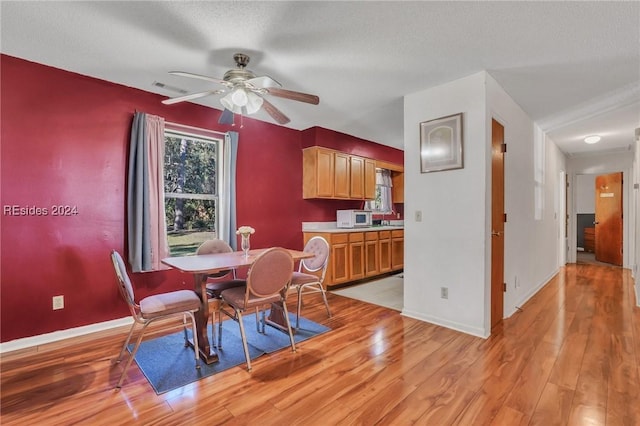 dining space featuring ceiling fan, sink, a textured ceiling, and light wood-type flooring