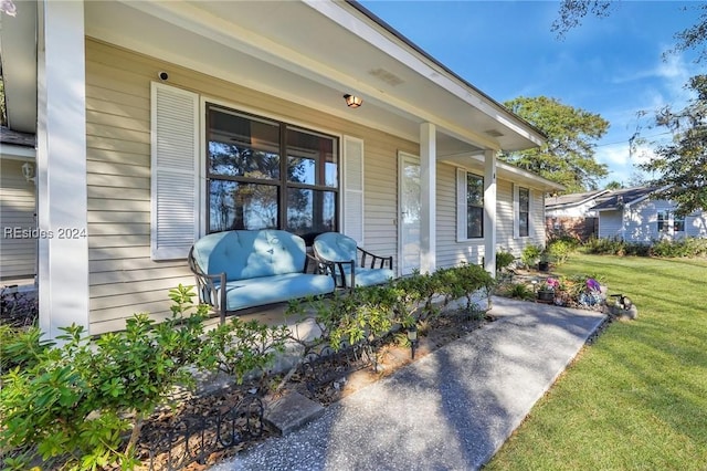 view of exterior entry with a lawn and a porch