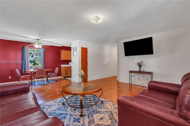 living room with ceiling fan, a textured ceiling, and light hardwood / wood-style floors