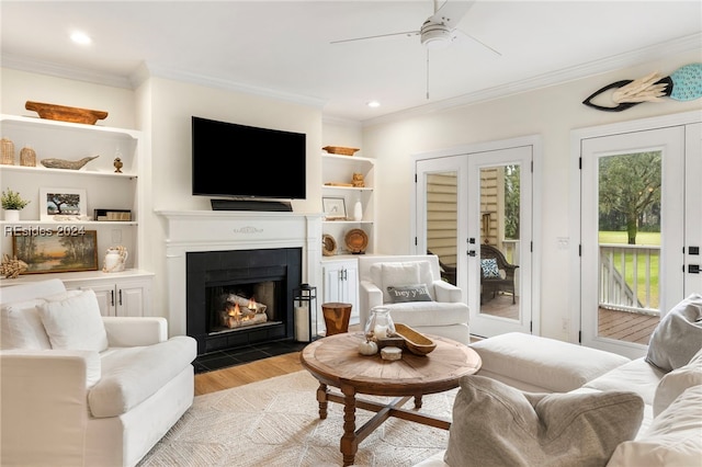 living room with a tile fireplace, crown molding, light wood-type flooring, and french doors