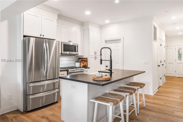 kitchen with appliances with stainless steel finishes, a breakfast bar, white cabinetry, light hardwood / wood-style floors, and a center island with sink