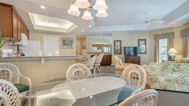 dining space with a raised ceiling, sink, carpet flooring, and ceiling fan with notable chandelier