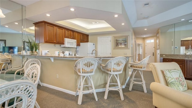 kitchen with pendant lighting, white appliances, carpet, light stone counters, and a raised ceiling