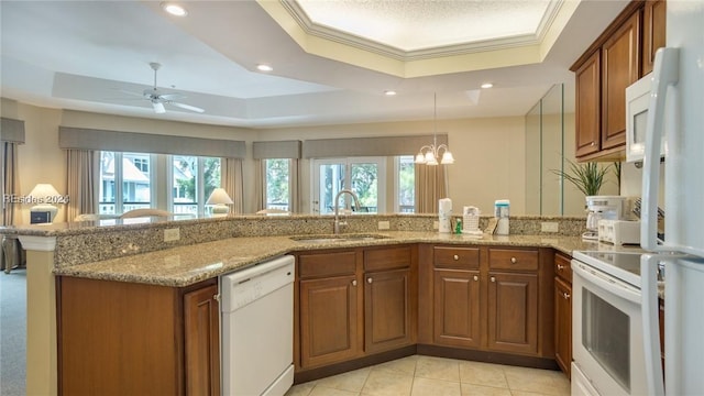 kitchen featuring sink, a tray ceiling, kitchen peninsula, white appliances, and light stone countertops