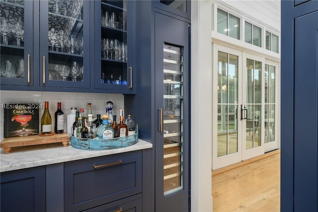 bar with tasteful backsplash, light hardwood / wood-style flooring, light stone countertops, and blue cabinetry