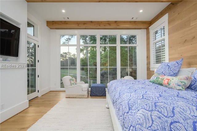 bedroom featuring beam ceiling, wooden walls, and light hardwood / wood-style floors