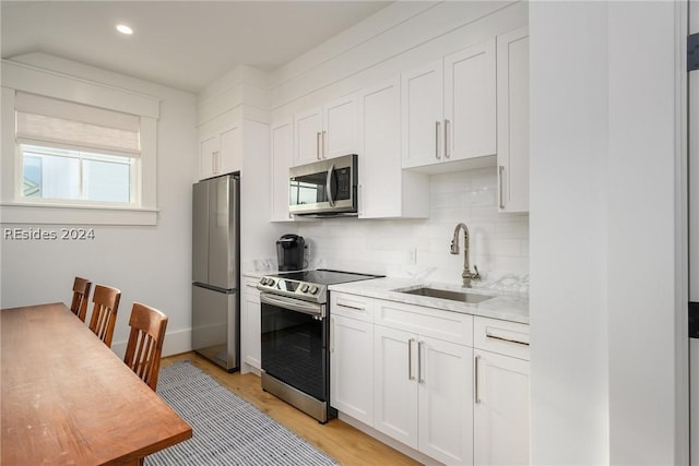 kitchen with white cabinetry, sink, light hardwood / wood-style floors, stainless steel appliances, and light stone countertops