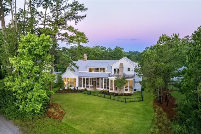 back house at dusk featuring a yard and a sunroom