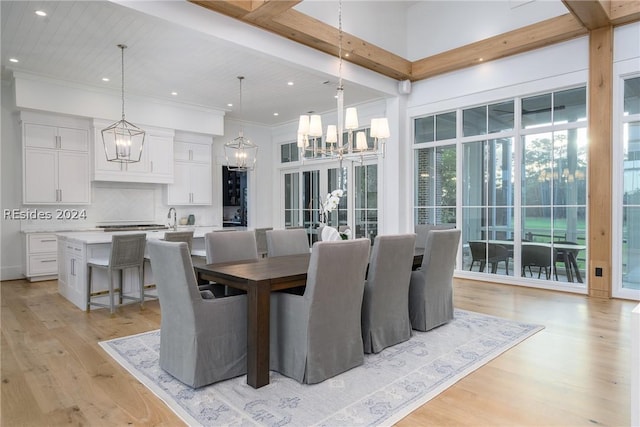 dining space featuring a notable chandelier, a towering ceiling, light hardwood / wood-style floors, and beamed ceiling