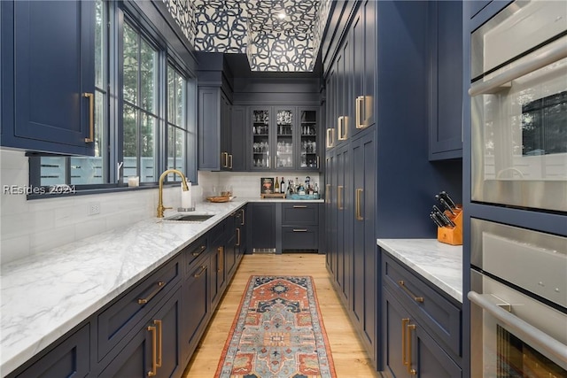 kitchen with light stone counters, sink, backsplash, and light hardwood / wood-style floors