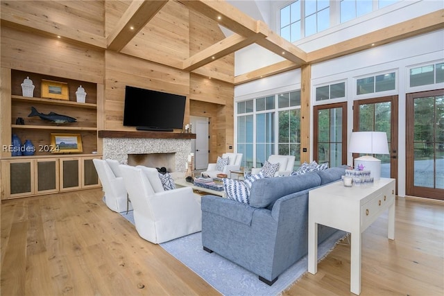 living room with beam ceiling, a towering ceiling, a fireplace, built in shelves, and light wood-type flooring