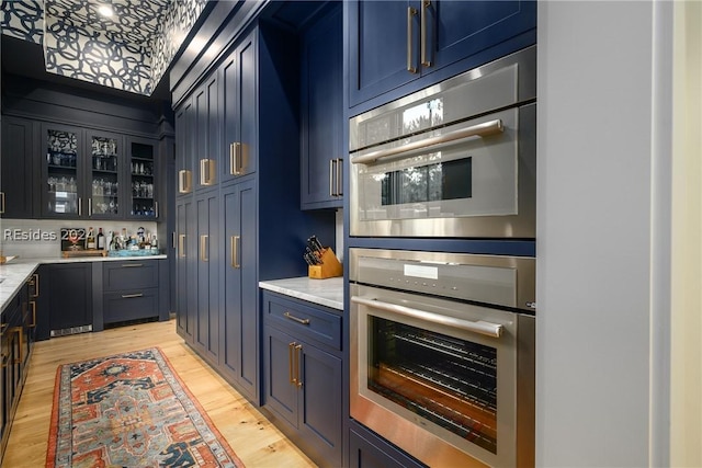 kitchen featuring double oven, light stone countertops, light hardwood / wood-style floors, and blue cabinetry