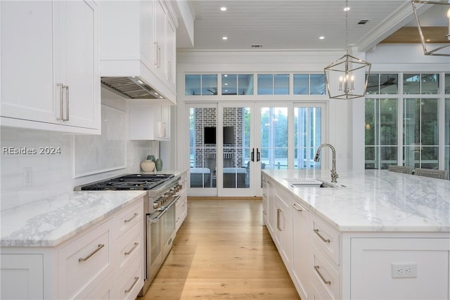 kitchen with high end range, sink, white cabinetry, and a center island with sink