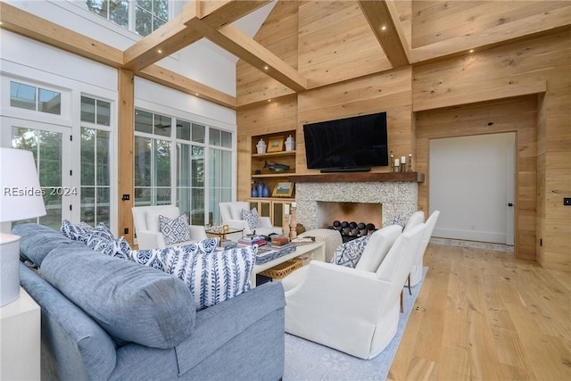 living room featuring light hardwood / wood-style flooring, wooden walls, beamed ceiling, and a high ceiling