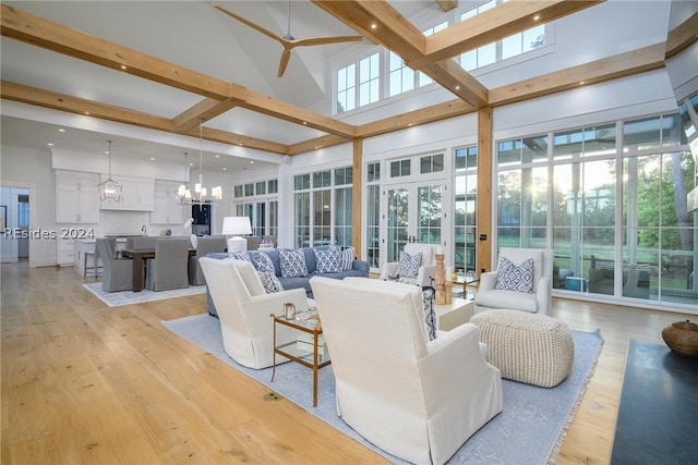 living room featuring beam ceiling, ceiling fan with notable chandelier, light hardwood / wood-style flooring, and a high ceiling