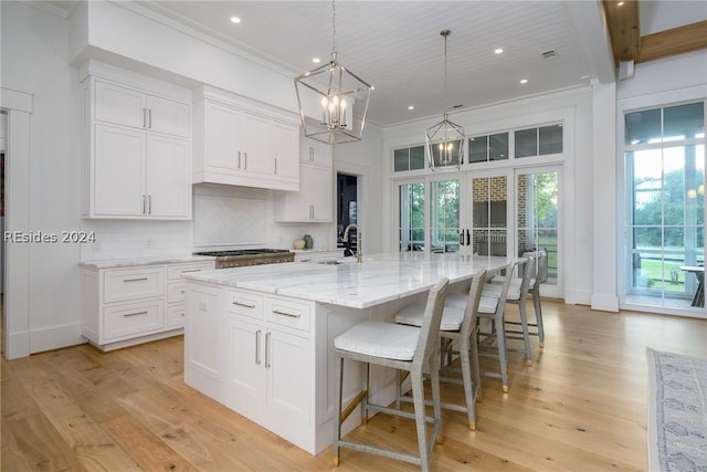 kitchen with white cabinetry, sink, hanging light fixtures, and a large island with sink