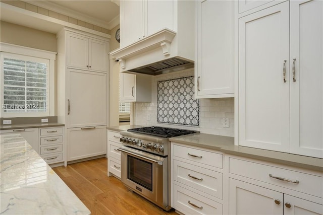 kitchen featuring custom exhaust hood, light stone counters, high end range, light hardwood / wood-style flooring, and decorative backsplash