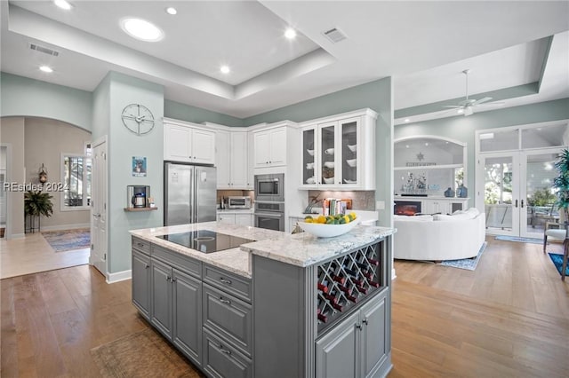 kitchen featuring gray cabinets, a raised ceiling, white cabinets, and appliances with stainless steel finishes