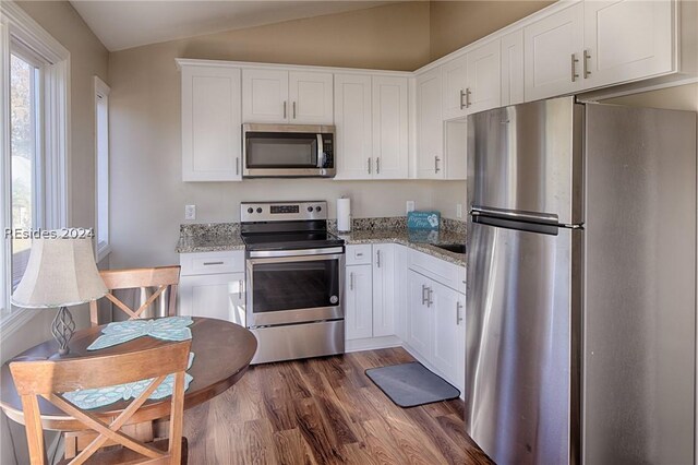 kitchen with lofted ceiling, appliances with stainless steel finishes, dark hardwood / wood-style floors, light stone countertops, and white cabinets