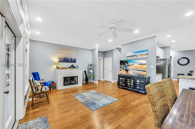 living room with a tiled fireplace, ornamental molding, ceiling fan, and light wood-type flooring