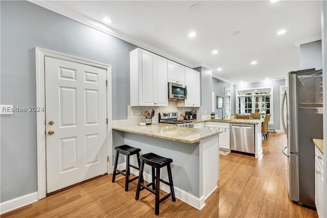 kitchen with a kitchen bar, white cabinetry, kitchen peninsula, stainless steel appliances, and light stone countertops