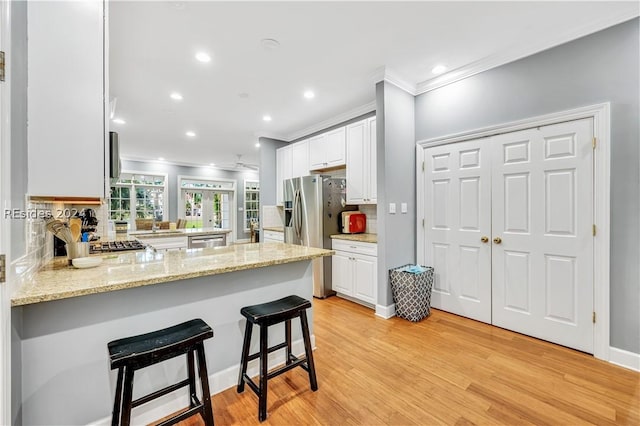 kitchen with backsplash, a kitchen breakfast bar, light stone counters, white cabinets, and kitchen peninsula