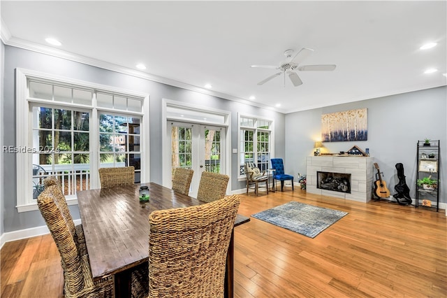 dining space featuring a tiled fireplace, light hardwood / wood-style flooring, french doors, and ceiling fan