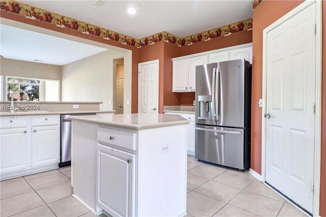 kitchen with sink, light tile patterned floors, appliances with stainless steel finishes, white cabinets, and a kitchen island