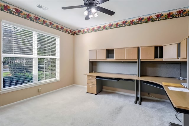 unfurnished office with a healthy amount of sunlight, built in desk, and light carpet