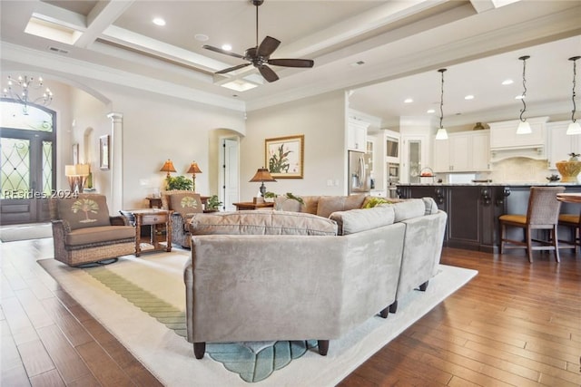 living room with beamed ceiling, dark hardwood / wood-style flooring, ornamental molding, coffered ceiling, and ceiling fan