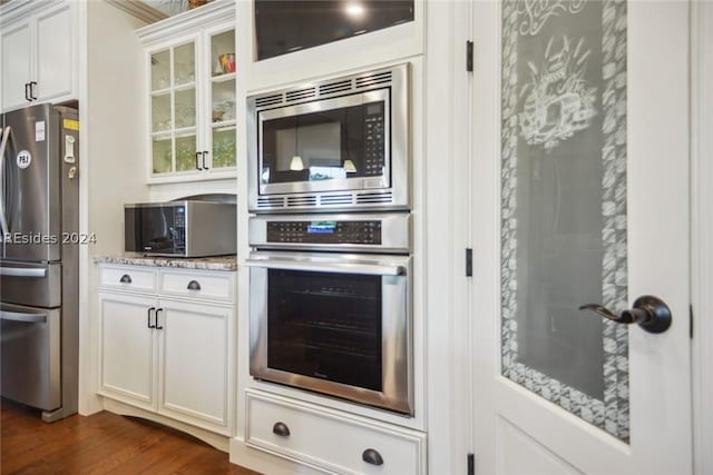 kitchen with light stone countertops, dark wood-type flooring, stainless steel appliances, and white cabinets