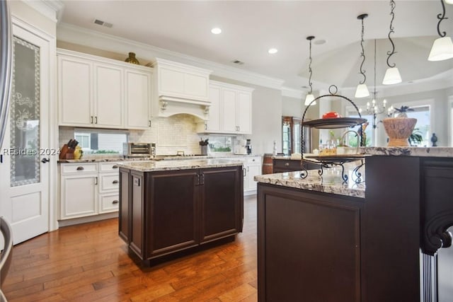 kitchen featuring hanging light fixtures, dark hardwood / wood-style floors, tasteful backsplash, light stone countertops, and a kitchen island