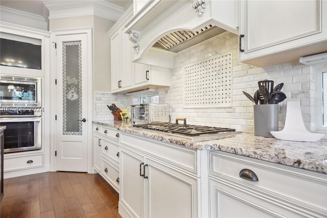 kitchen featuring appliances with stainless steel finishes, white cabinetry, backsplash, custom exhaust hood, and light stone countertops