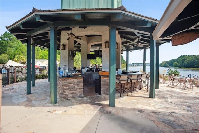 view of patio featuring a gazebo, ceiling fan, exterior bar, and a water view