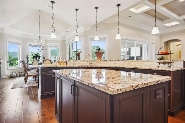 kitchen with a spacious island, dark brown cabinetry, light stone counters, decorative light fixtures, and dark hardwood / wood-style floors