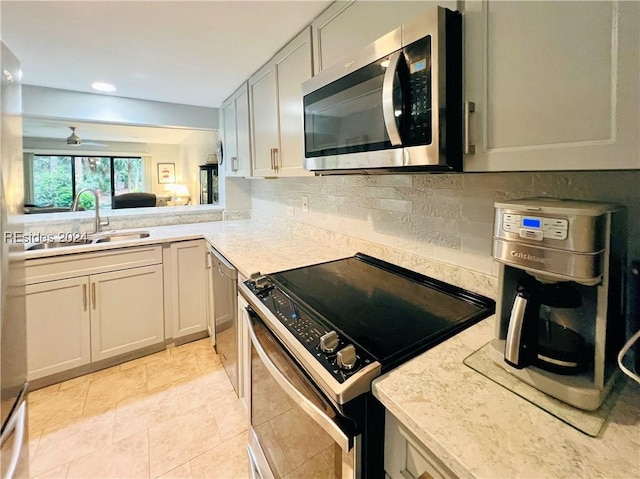 kitchen featuring sink, ceiling fan, appliances with stainless steel finishes, light stone counters, and light tile patterned flooring