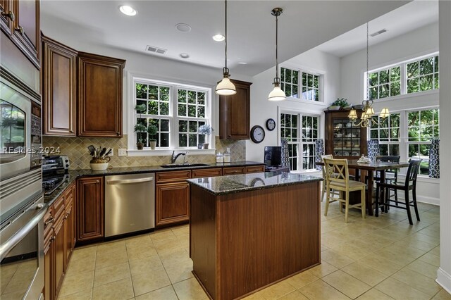 kitchen with light tile patterned floors, appliances with stainless steel finishes, hanging light fixtures, a center island, and dark stone counters