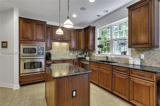 kitchen featuring appliances with stainless steel finishes, decorative light fixtures, sink, dark stone countertops, and a center island