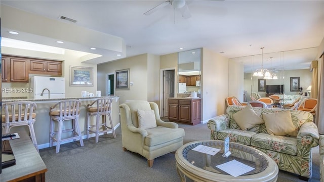 carpeted living room featuring sink and ceiling fan with notable chandelier