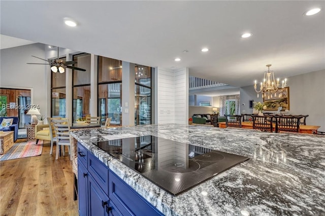 kitchen with ceiling fan with notable chandelier, dark stone counters, light hardwood / wood-style floors, blue cabinetry, and black electric cooktop