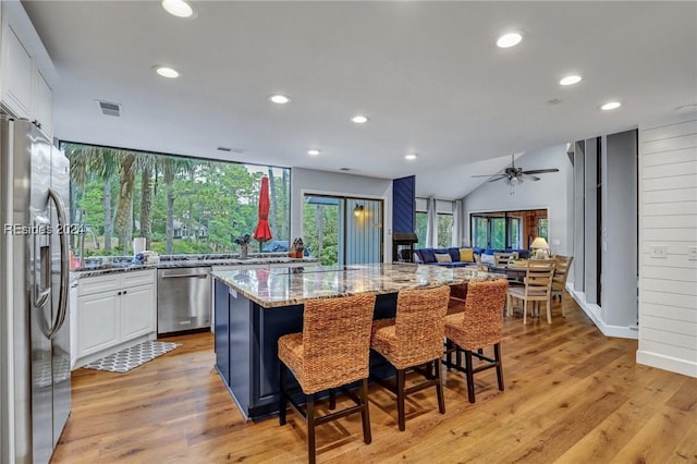 kitchen featuring stainless steel appliances, a kitchen breakfast bar, a center island, light stone counters, and white cabinets