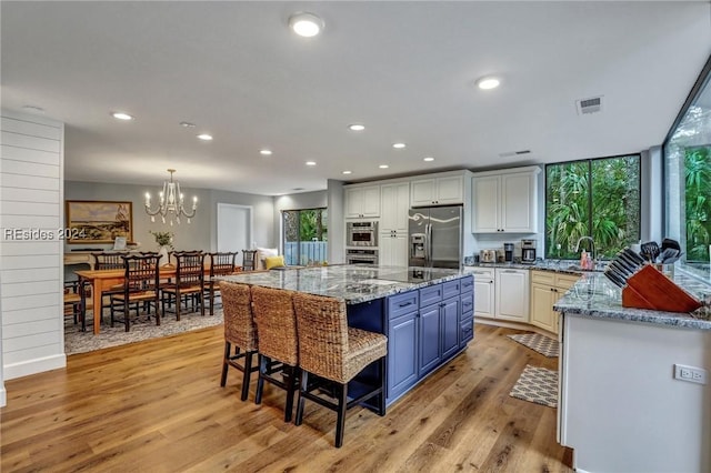 kitchen with stainless steel appliances, blue cabinetry, a large island, and light wood-type flooring