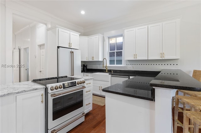 kitchen with white cabinetry, a breakfast bar area, premium appliances, and dark stone counters