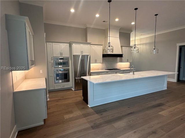 kitchen with sink, appliances with stainless steel finishes, hanging light fixtures, a center island with sink, and custom exhaust hood