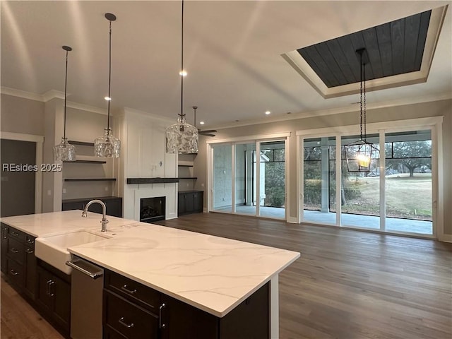 kitchen with sink, hanging light fixtures, light stone counters, crown molding, and a center island with sink