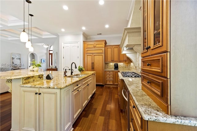 kitchen featuring coffered ceiling, sink, light stone counters, a large island with sink, and ornamental molding